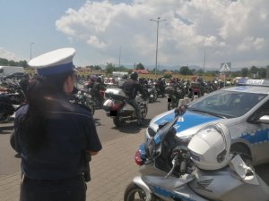tyłem stoi policjantka obok niej radiowóz w tle motocykliści na motorach