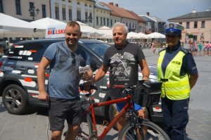 na tle wozu radia bielsko stoi redaktor policjantka i rowerzysta z rowerem w tle rynek i miasto
