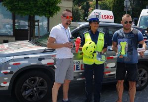 na tle wozu radia bielsko stoi policjantka z redaktorami którzy trzymają przedmioty poprawiające bezpieczeństwo kierowców jednośladów