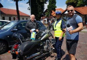 na tle motocykla stoi motocyklista trzyma szelki obok stoi policjantka i redaktor radia bielsko