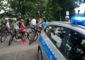 fragment radiowozu obok policjantka i rowerzyści