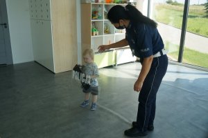 zdjęcie wykonane w sali przedszkola policjantka stoi obok dziecka któe trzyma tarcze policyjną