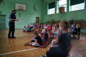 zdjęcie zrobione w sali gimnastycznej policjantka stoi bokiem dzieci siedzą na ławkach