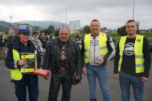 stoi policjantka obok niej motocykliści policjantkami motocykliści trzymają odblaskowe szelki w tle inni motocykliści