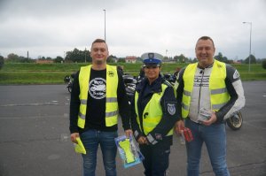 stoi policjantka obok niej motocykliści motocykliści trzymają przekazane przez policjantkę odblaskowe szelki