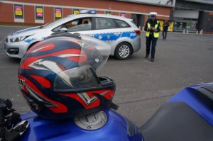 na pierwszym planie kask motocyklowi i fragment motocykle w tle radiowóz i policjantka