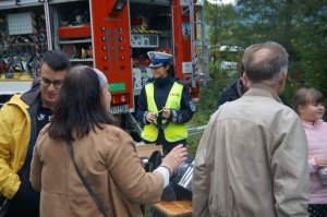 na pierwszym planie tyłem stoją osoby przy stoisku policyjnym w tle policjantka i wóz strażacki