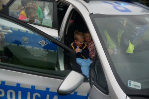zdjęcie zrobione na zewnątrz dzieci siedzą w radiowozie są obok radiowozu radiowóz zaparkowany jest na trawie