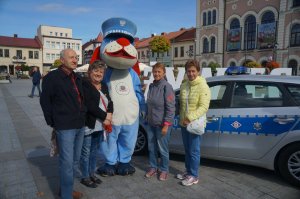 osoby stoją obok sznupka obok zaparkowany radiowóz w tle widać miasto