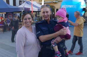 policjantka trzyma na rękach dziecko obok stoi kobieta w tle miasto