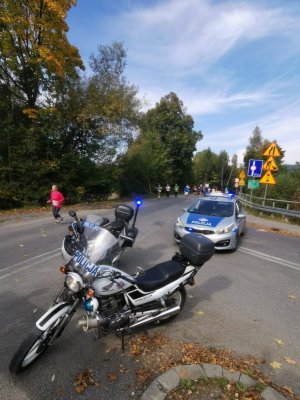 na pierwszym planie policyjny motor i radiowóz w tle widocznu biegacze