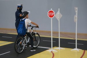 uczeń na rowerze na miasteczku ruchu drogowego zatrzymuje się przed znakiem stop obok policjantka
