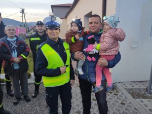 policjantka obok niej stoi mężczyzna który trzyma na rękach dzieci w tle inne osoby