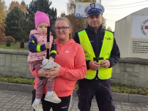 stoi policjant obok niego kobieta która trzyma na rękach dziecko