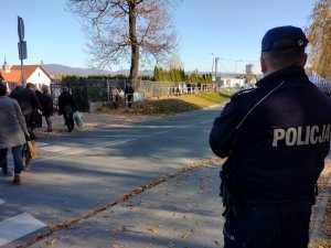 policjant stoi tyłem w tle cmentarz i ludzie