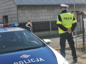 fragment radiowozu obok stoi policjant w tle biegnący mezczyzna