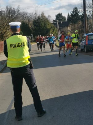 na pierwszym planie stoi policjant w tle biegacze