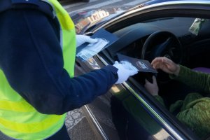 fragment policjantki i kierowcy który siedzi w samochodzie policjantka wręcza mu ulotki i zawieszkę