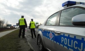 grafika poglądowa na pierwszym planie radiowóz w tle dóch policjanów oraz droga