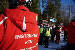 instruktor narciarstwa stojący tyłem fragment osoby w tle stok narciarski