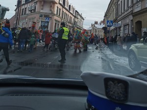 zdjęcie zrobione z wnętrza radiowozu na pierwszym planie policyjna czapka w tle ulica po której idą kolędnicy