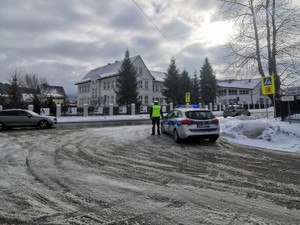 na skrzyżowaniu zaparkowany radiowóz okok którego stoi policjant w tle budynki i droga po której jadą samochody