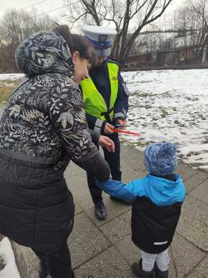 policjantka wręcza odblask dziecku obok stoi matka