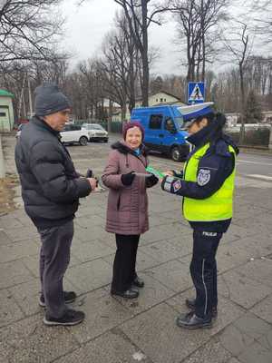 policjantka wręcza odblask starszej kobiecie obokstoi męzczyzna w tle ulica