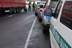 fragmenty samochodów służb zaparkowanych zwdłuż drogi po drugiej stronie drogi zaparkowany tir