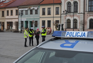 na pierwszym planie fragment radiowozu z napisem policja w tle stoją policjanci pracownik word oraz kobieta