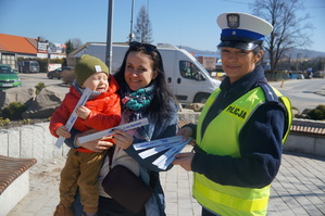 obok siebie stoi policjantka oraz kobieta z dzieckiem wszyscy trzymają odblaski w tle ulica