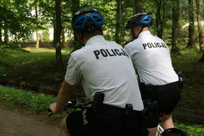 grafika poglądowa dwóch policjantów na rowerach jedzie przez park