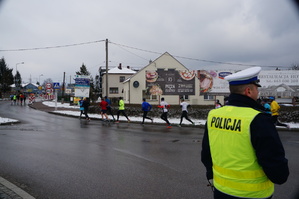 po prawej stronie zdjęcie na drodze stoi policjant dalej widoczna ulica z biegaczami