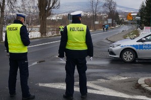 policjanci stoją na drodze obok radiowóz w tle biegnący biegacze