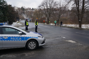 zaparkowany roadiowóz obok niego stoją policjanci w tle ulica i biegacze