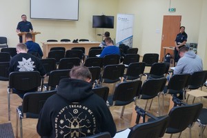 zdjęcie zrobione w sali podczas pisania przez uczestników testu uczniowie siedzą i piszą test obok stoi dwóch polkicjantów