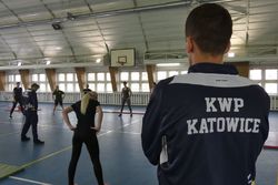 zdjęcie poglądowe egzaminator stoi tyłem na założony bluzę z napisem KWP Katowice w tle ćwiczący