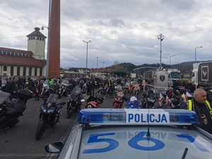 na pierwszym planie fragment radiowozu z napisem policja w tle motory i motocykliści