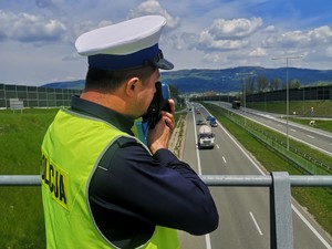 fragment policjanta stoi tyłem trzyma urządzenie trucam2 w tle ulica i krajobraz policjant stoi na wiadukcie