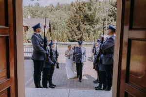 zdjęcie zrobione z wnętrza kościoła do kościoła wchodzi młoda para na schodach stoją policjanci z kompanii honorowej