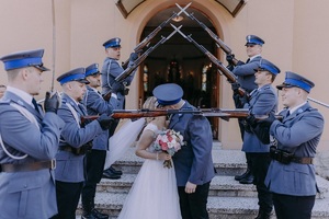 Na schodach stoją policjanci z kompanii honorowej na schodach stoi młoda para która całuje się