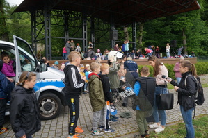 dzieci w czasie przymierzania policyjnego wyposażenia w tle radiowóz i scena