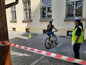 z prawej strony stoi policjantka obok wyznaczony tor rowerowy po którym jedzie roiwerzysta