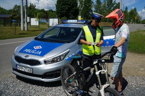 policjantka stoi obok rowerzysty obok zaparkowany radiowóz