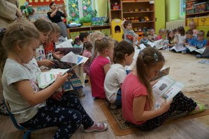 dzieci siedzą na dywanie i oglądają książeczki
