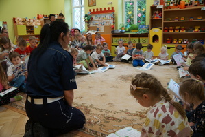 policjantka kuca na dywanie dzieci siedzą i oglądają ksiązeczki policjantka omawia ich treśc