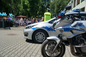 na pierwszym planie policyjny motocykl radiowóz i policjant stojący tyłem w tle piknik
