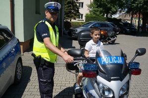 chłopczyk siedzi na policyjnym motocyklu obok stoi policjant