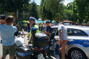 policyjny motocykl i radiowóz obok stoją policjantka i policjant oraz osoby oglądające go