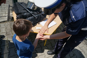 policjantka pokazuje dziecku w jaki sposób zabezpiecza się odciski linii papilarnych